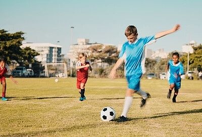 Barn spelar fotboll på en gräsplan i fullt solsken